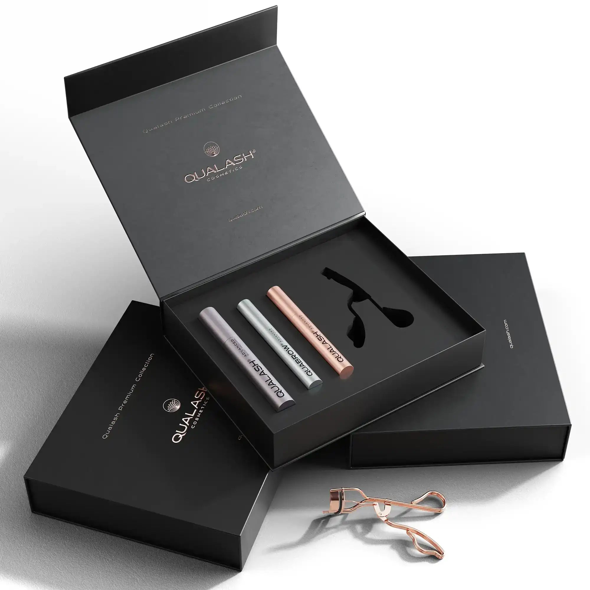 A black gift box containing three tubes of cosmetic products and a rose gold eyelash curler.