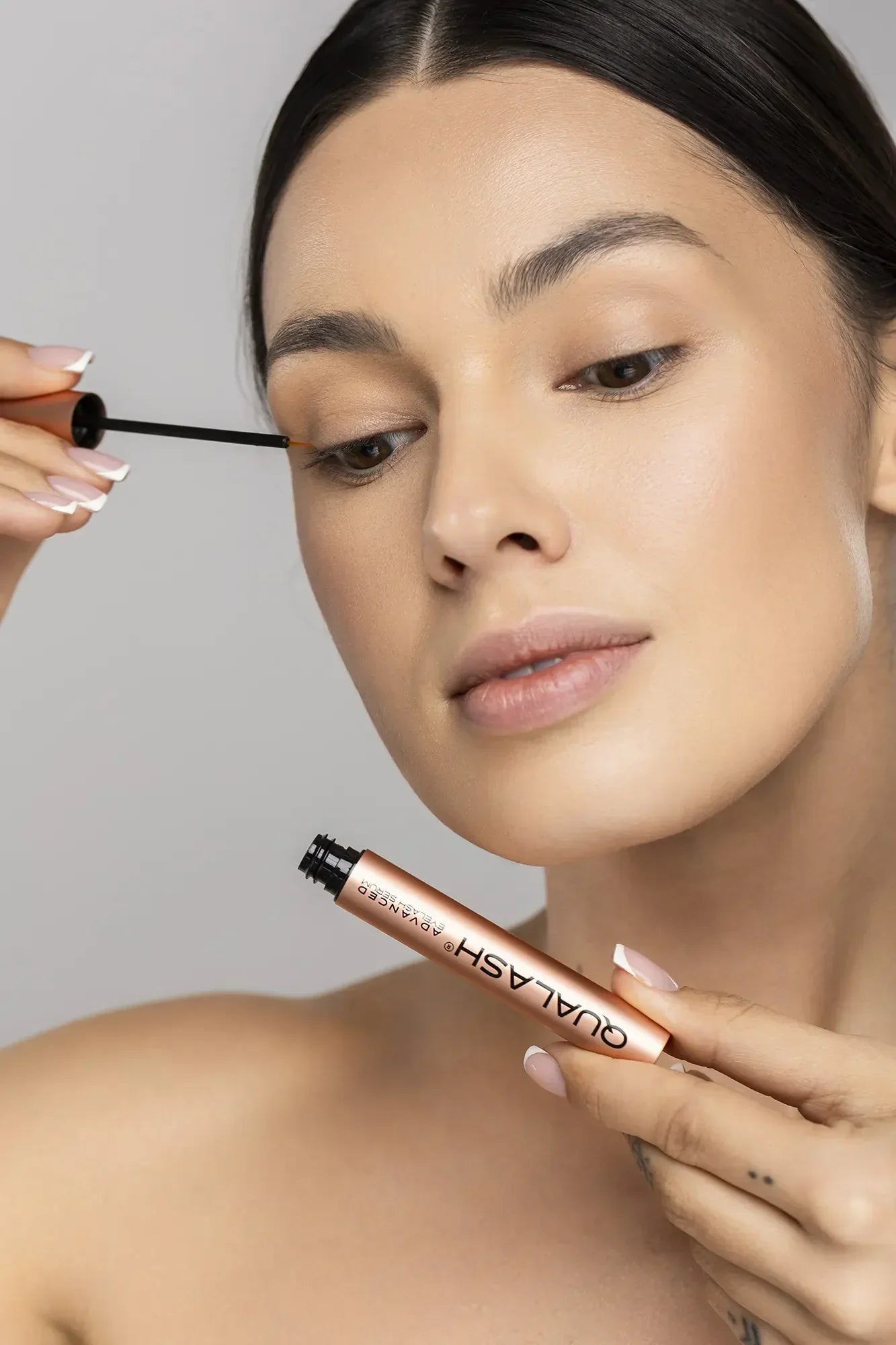 Woman applying QUALASH Advanced Eyelash Serum to her upper lash line