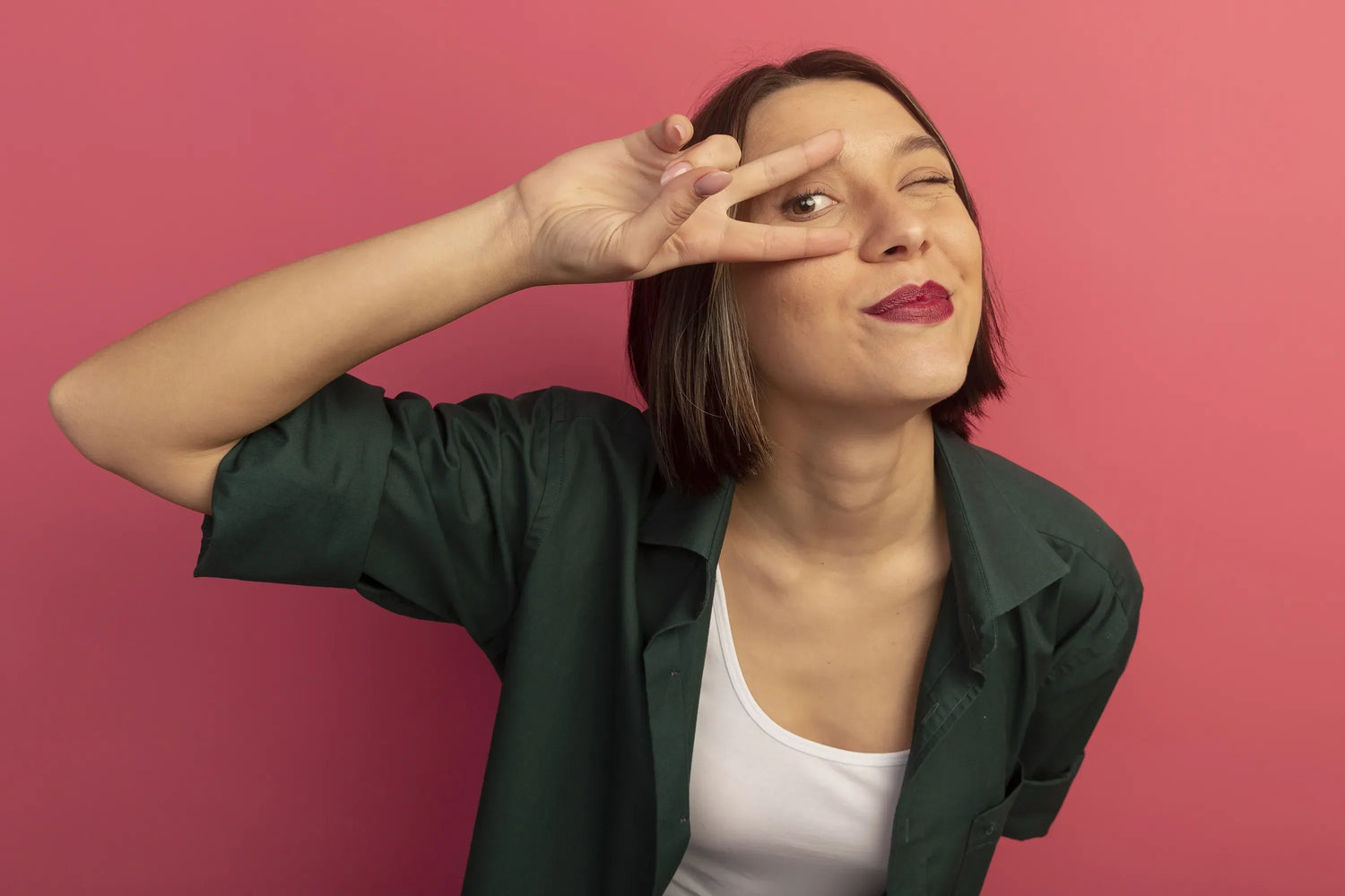 Confident woman over 40 showing eye area with a playful gesture against pink background
